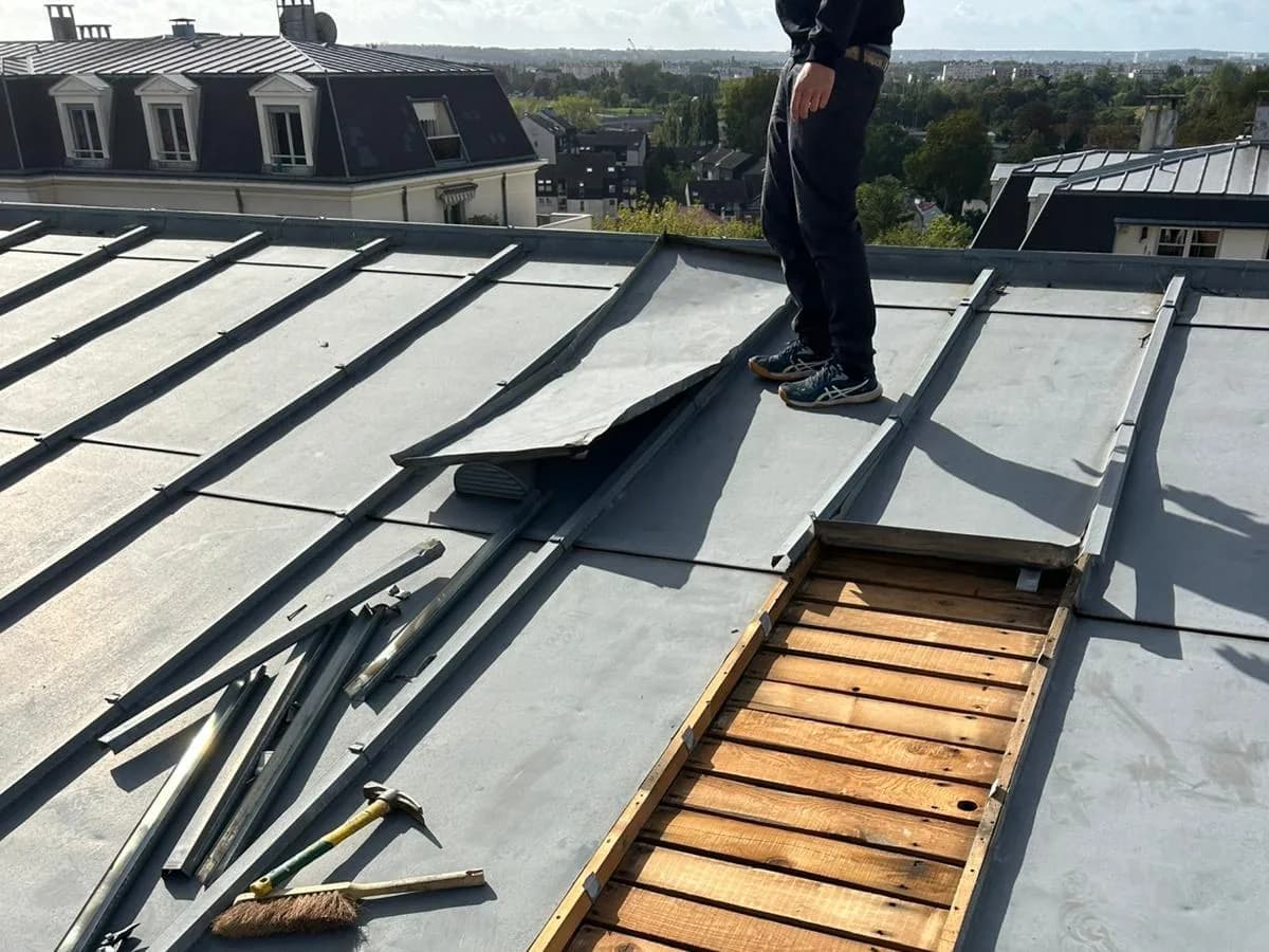 Ouverture dans une toiture en zinc laissant apparaître le voligeage en bois, outils posés à côté